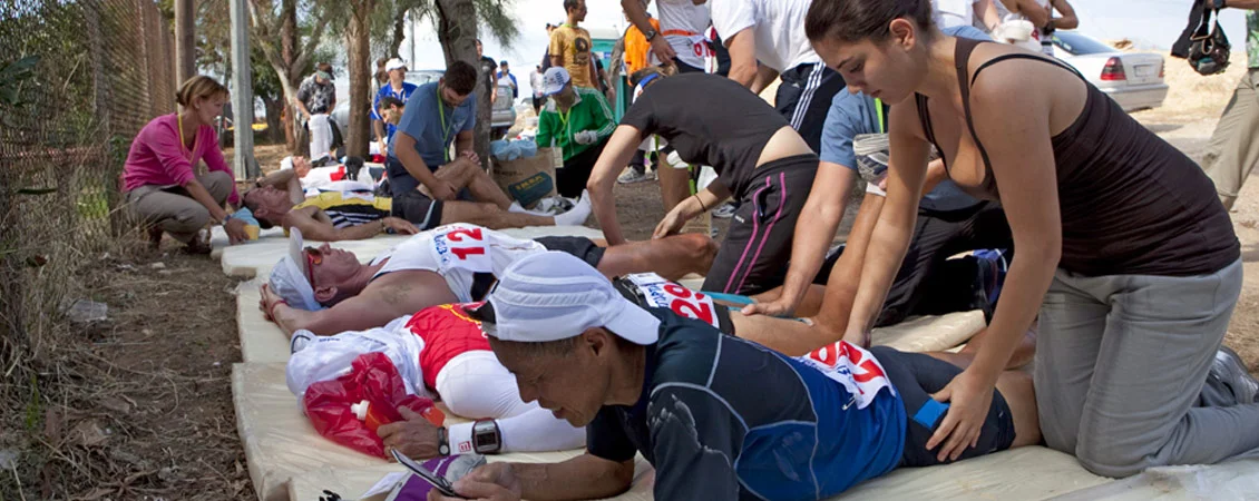 Equipo de fisioterapeutas realizando masajes de descarga y asistencia muscular a corredores de la ultramaratón Spartathlon en un puesto de control.
